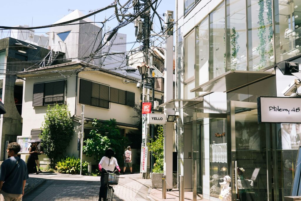 街並みの写真。右側にガラス張りの店(白いオブジェが置かれ高級感のある雰囲気)、奥に一般住宅があり、歩行者が数名、手前に自転車に乗っている人が写っている。