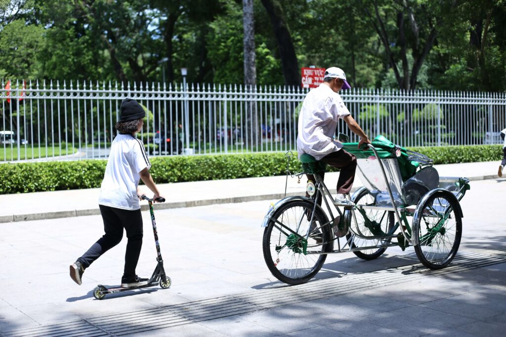 三輪自転車に乗った大人と電動キックボードになった子どもが誘導ブロックの側を走行している写真。