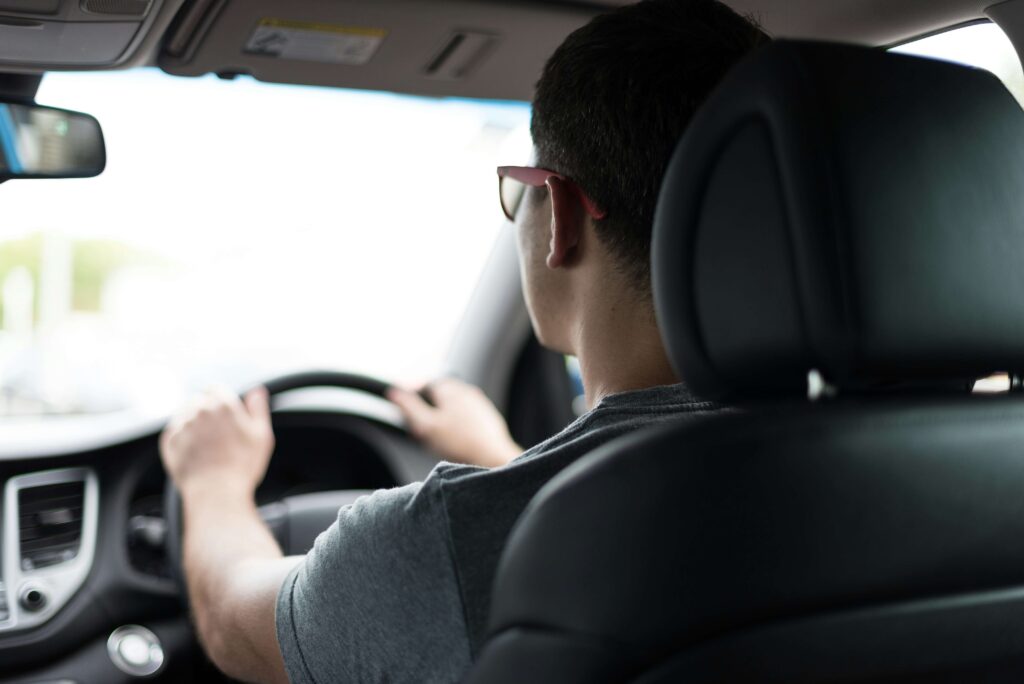 眼鏡を掛けて車を運転している男性を後ろ姿を車内で撮った写真。